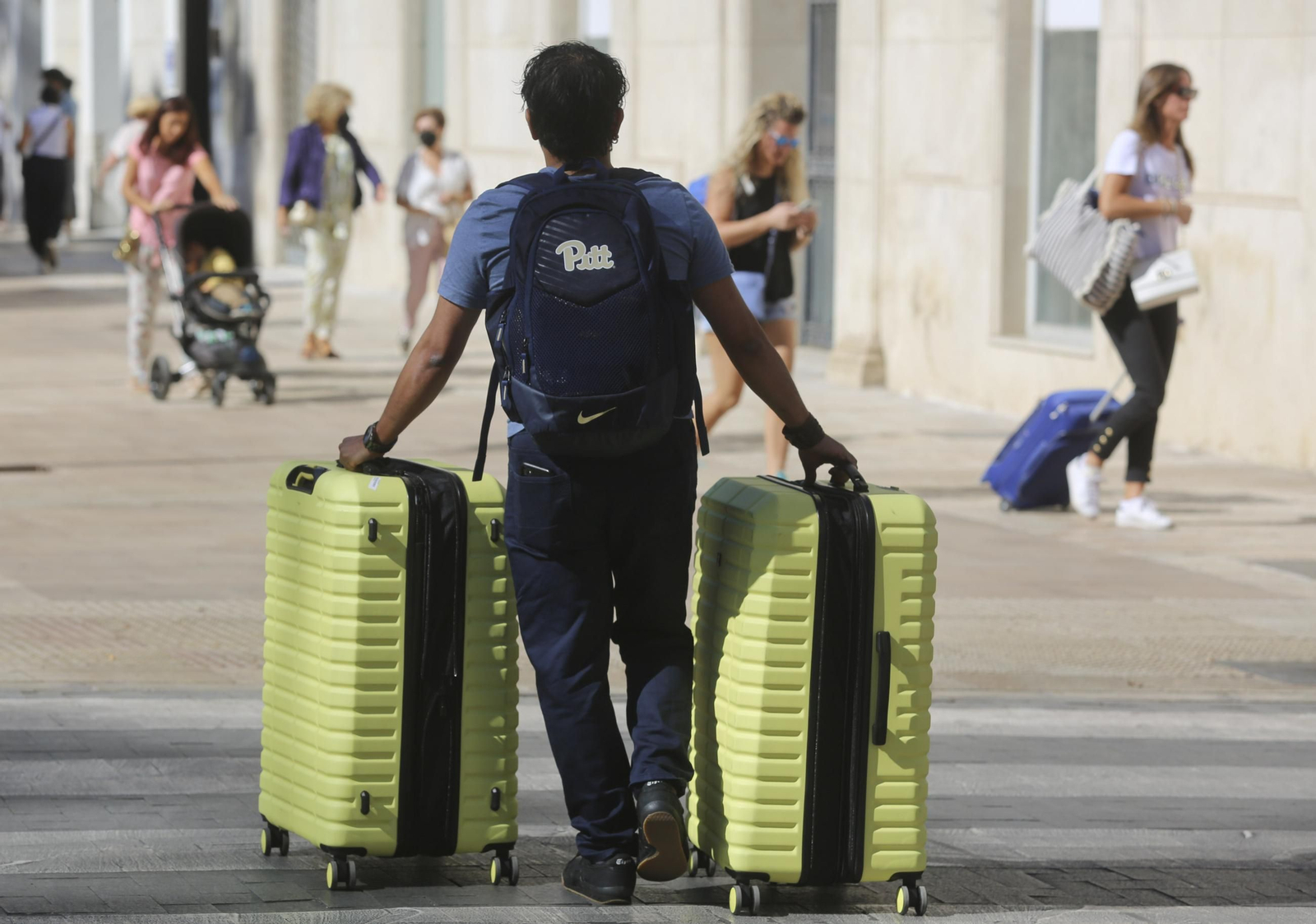 Un hombre porta dos baúles rodantes en una calle de Málaga.