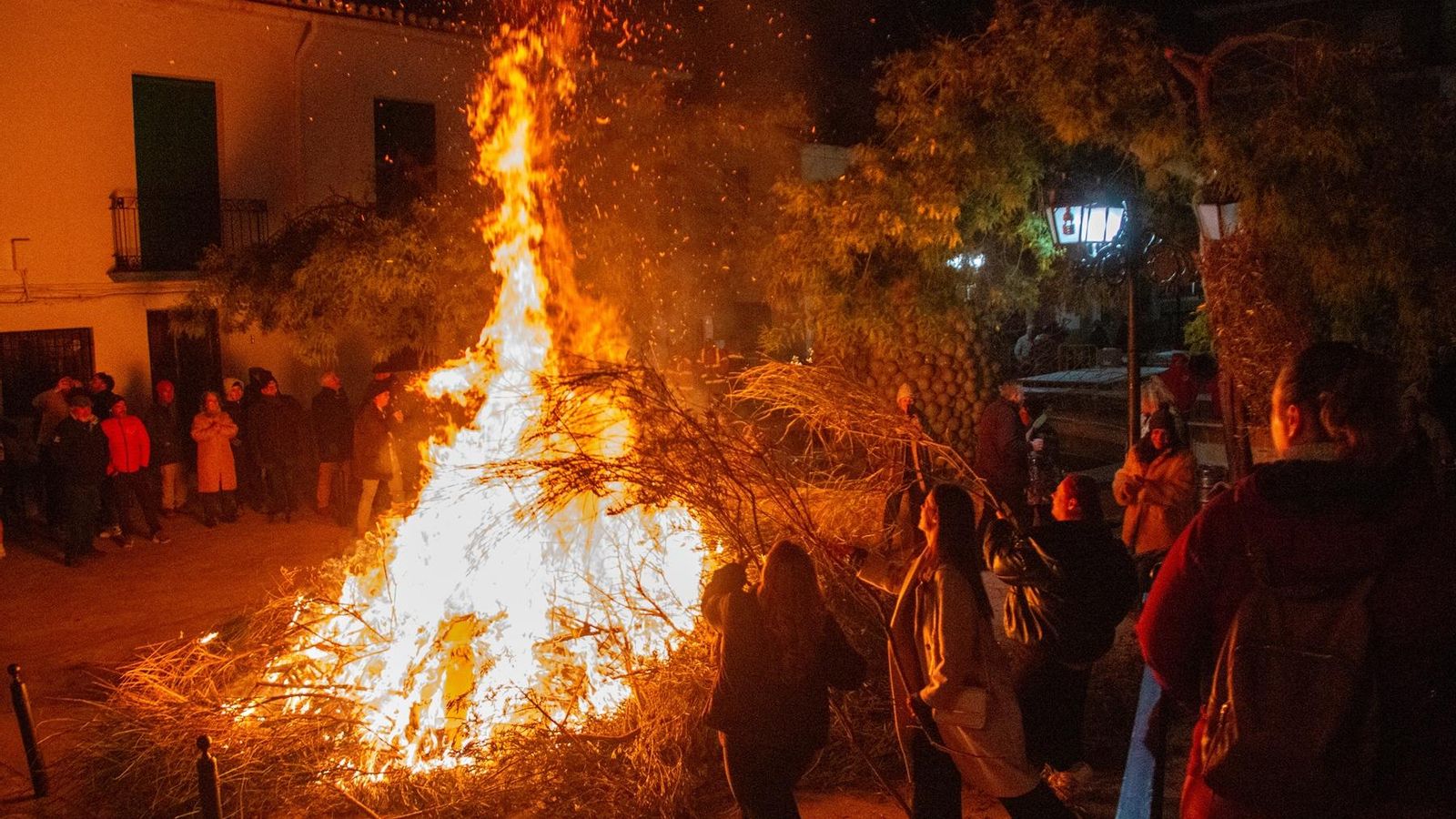 Varias personas se acercan al fuego para echar su rama de gayomba