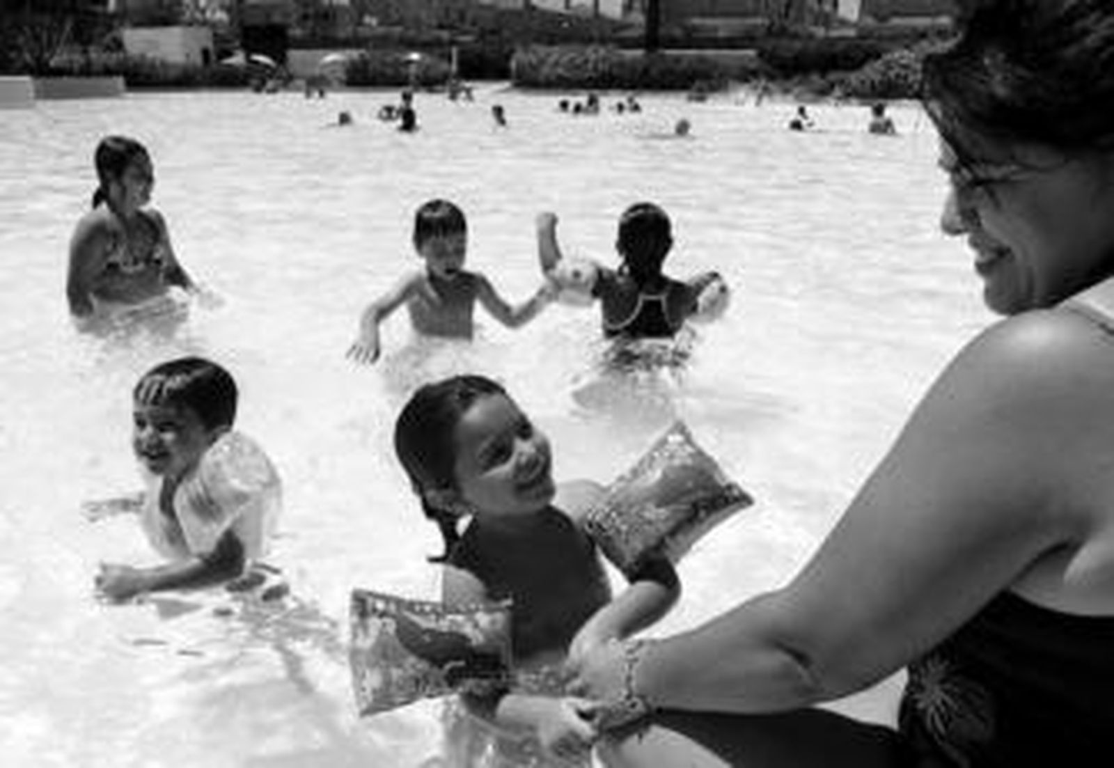 Unos pequeños juegan en el agua bajo la atenta mirada de su madre.