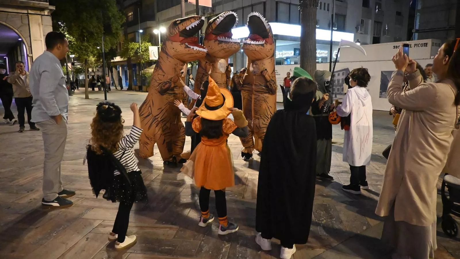 Varios niños acercándose al grupo de jóvenes disfrazados de dinosaurios.