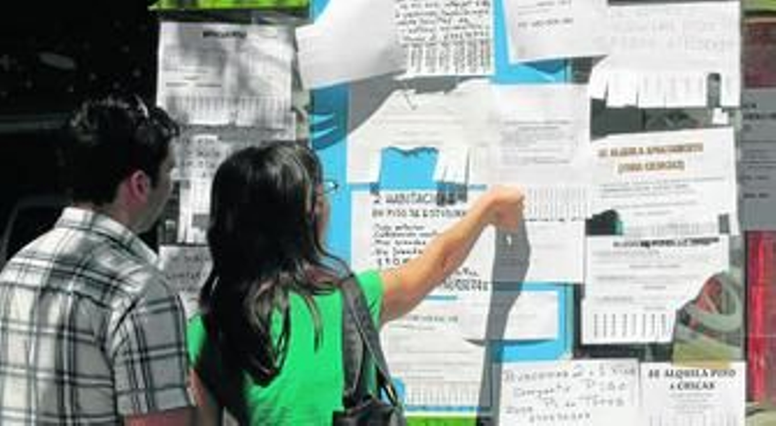 Dos estudiantes miran carteles con ofertas de pisos.