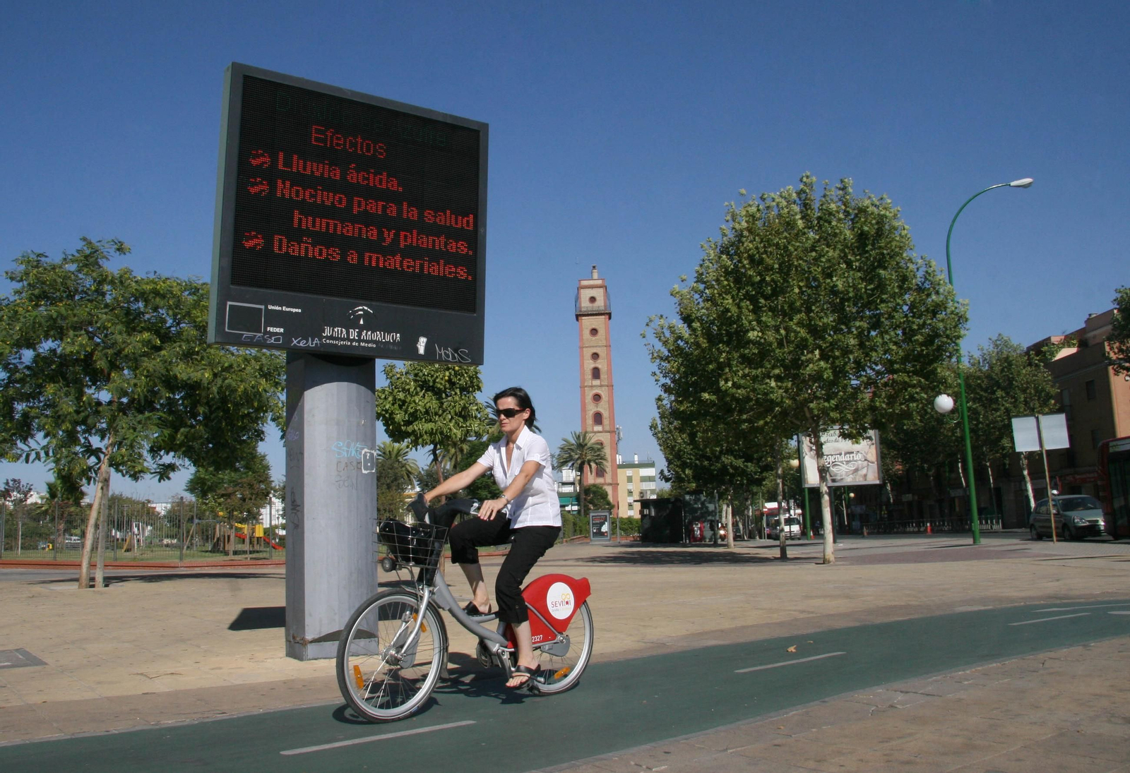 Una mujer conduce una bicicleta en Sevilla delante de un panel señalizador de contaminantes. Una mujer conduce una bicicleta en Sevilla delante de un panel señalizador de contaminantes.