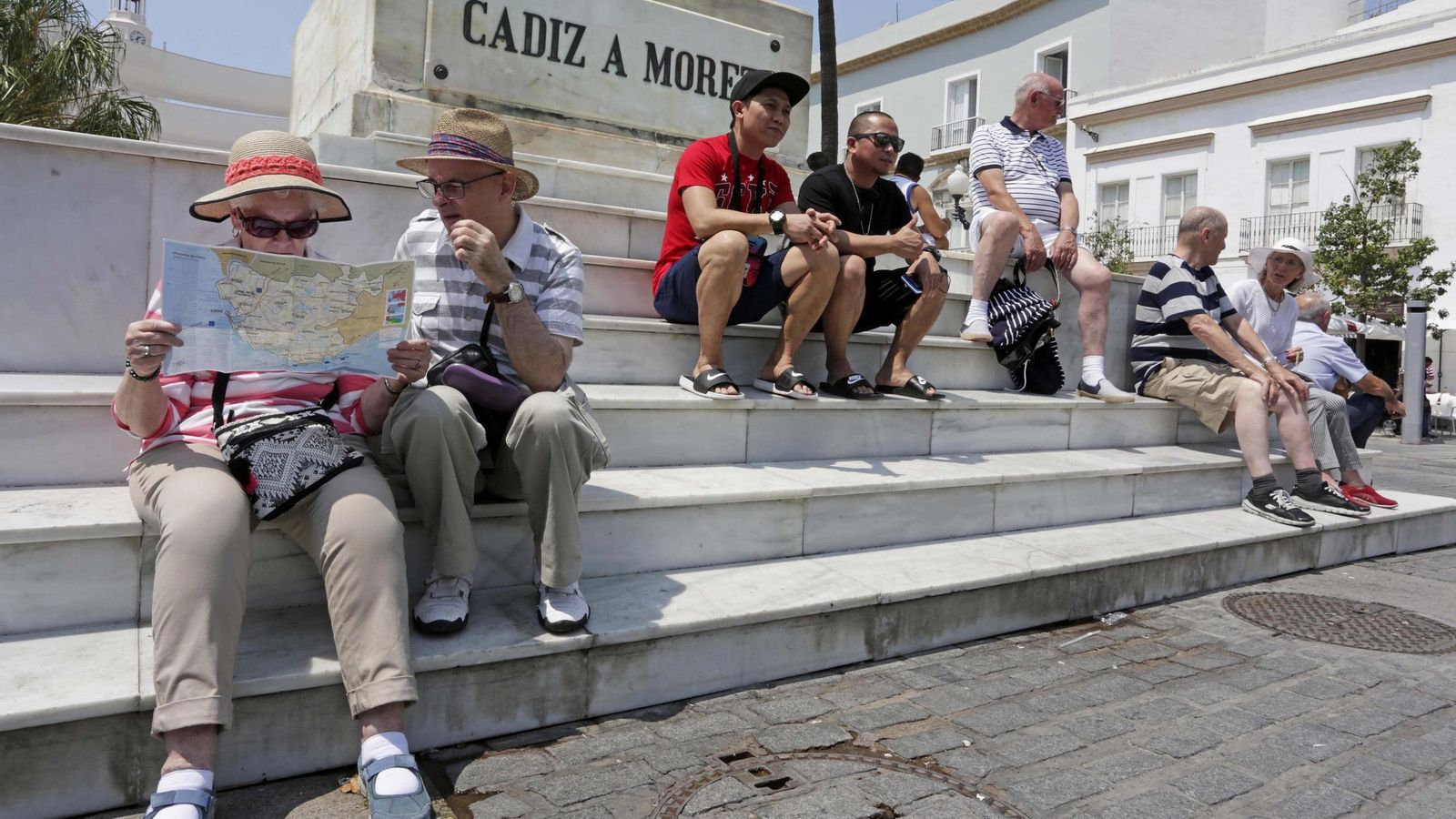 Turistas llegados por mar y por tierra, sentados a los pies de la estatua de Moret, en la plaza de San Juan de Dios de Cádiz