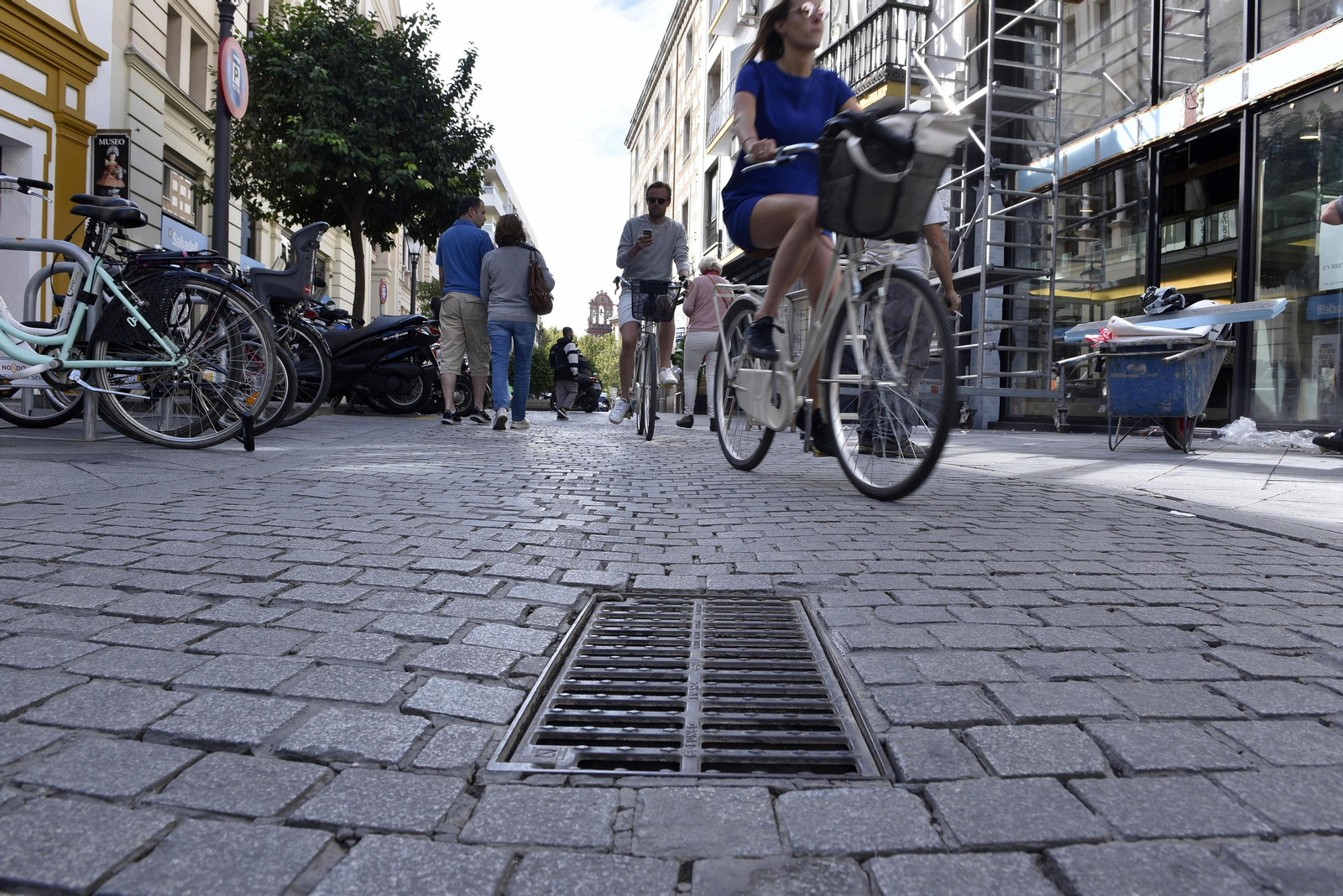 Dos ciclistas pasan junto a una alcantarilla del centro de Sevilla.
