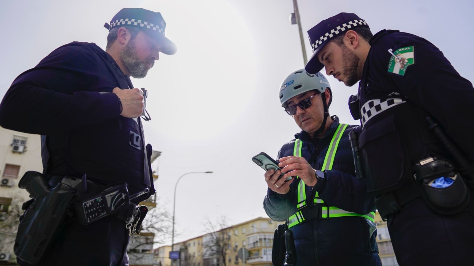 Un usuario con casco y prendas reflectantes enseña una documentación en el móvil a dos agentes.