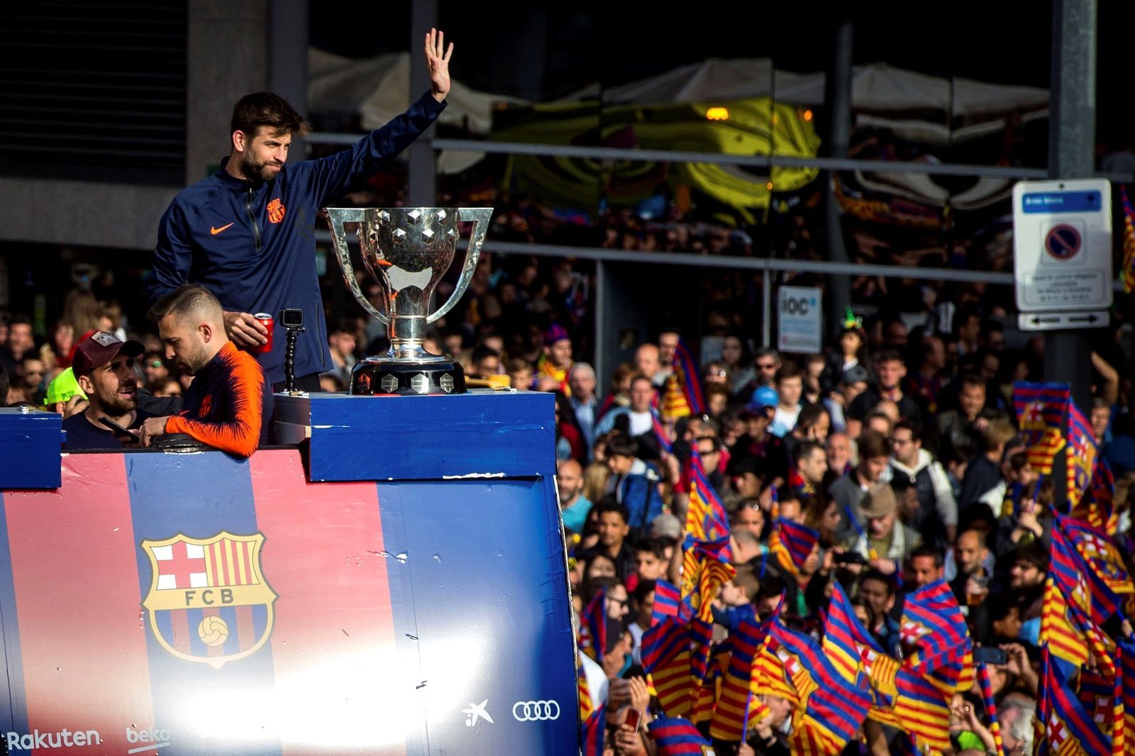 El capitán Gerard Piqué saluda a la afición desde el autobús descapotable con el trofeo de La Liga presidiendo la escena.