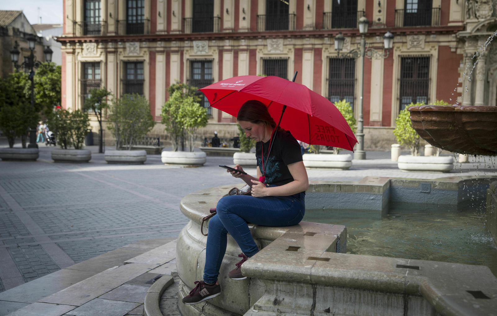 Una guía turística espera la llegada de clientes en el centro de Sevilla, casí vacío de visitantes.