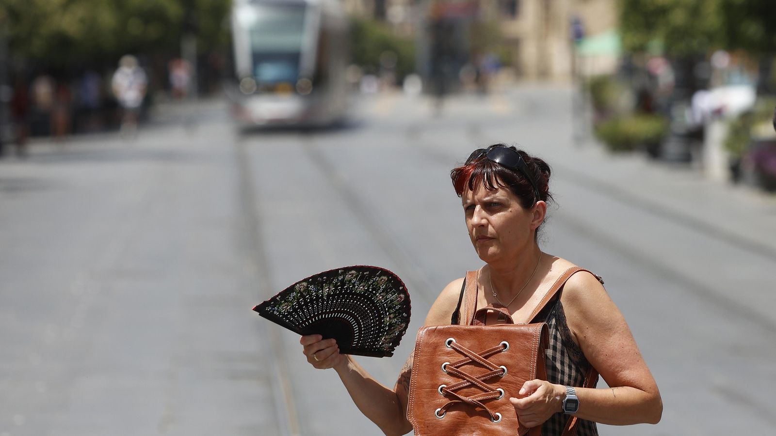 Una mujer se abanica a pleno sol en la Avenida de la Constitución.