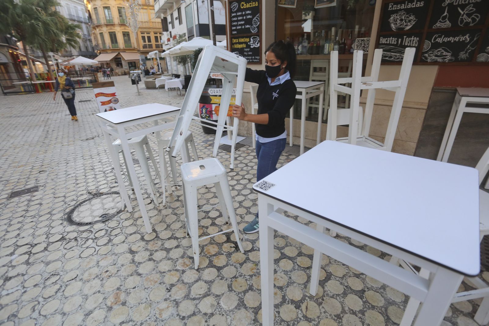 La empleada de un bar del Centro de Málaga recoge las mesas.