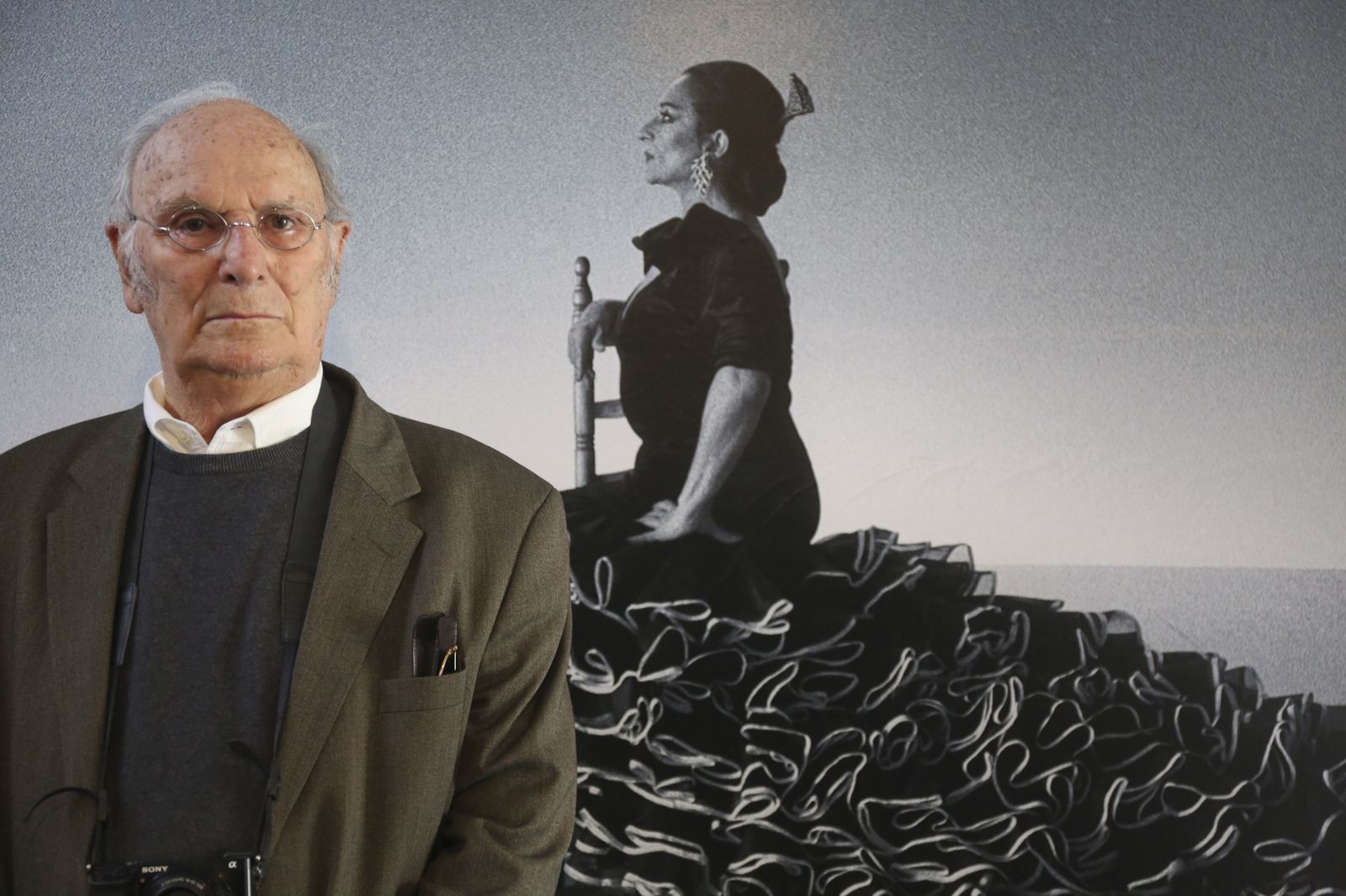 Carlos Saura con una imagen de Lola Flores en 'Sevillanas' detrás.