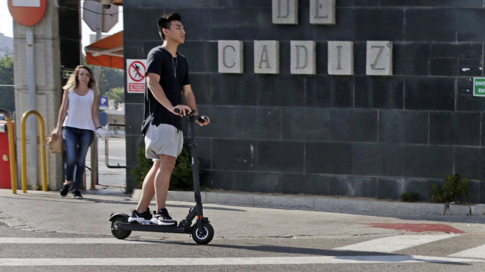 Un usuario de un patinete eléctrico pasando por delante de uno de los accesos al puerto de Cádiz