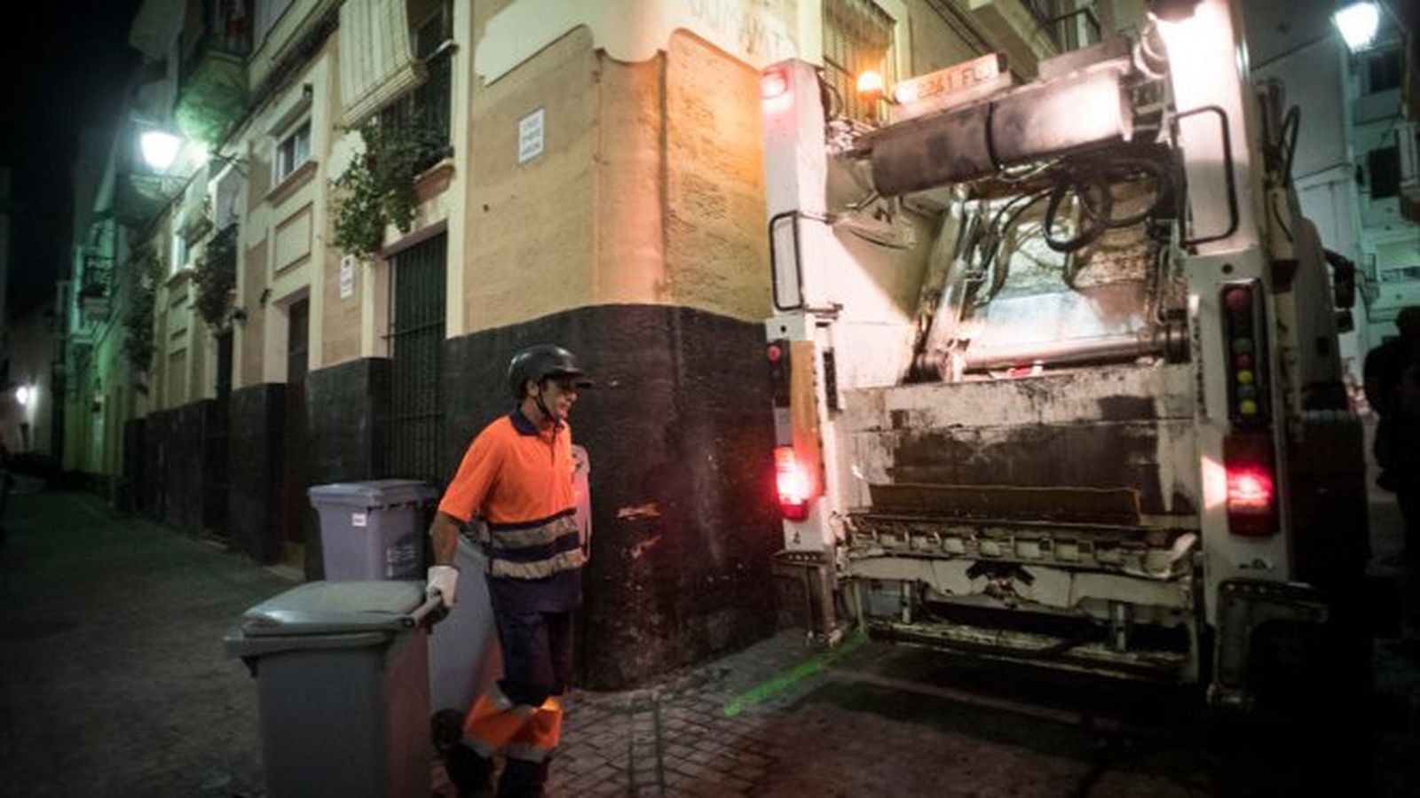 Un operario del servicio de recogida de basura transporta un contenedor hacia el camión.