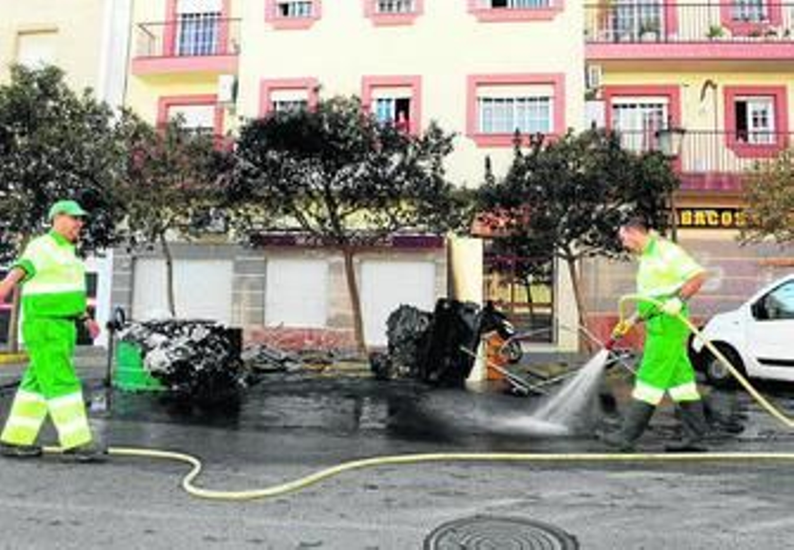 Operarios intentan limpiar la zona, donde se ven los contenedores y muebles quemados.