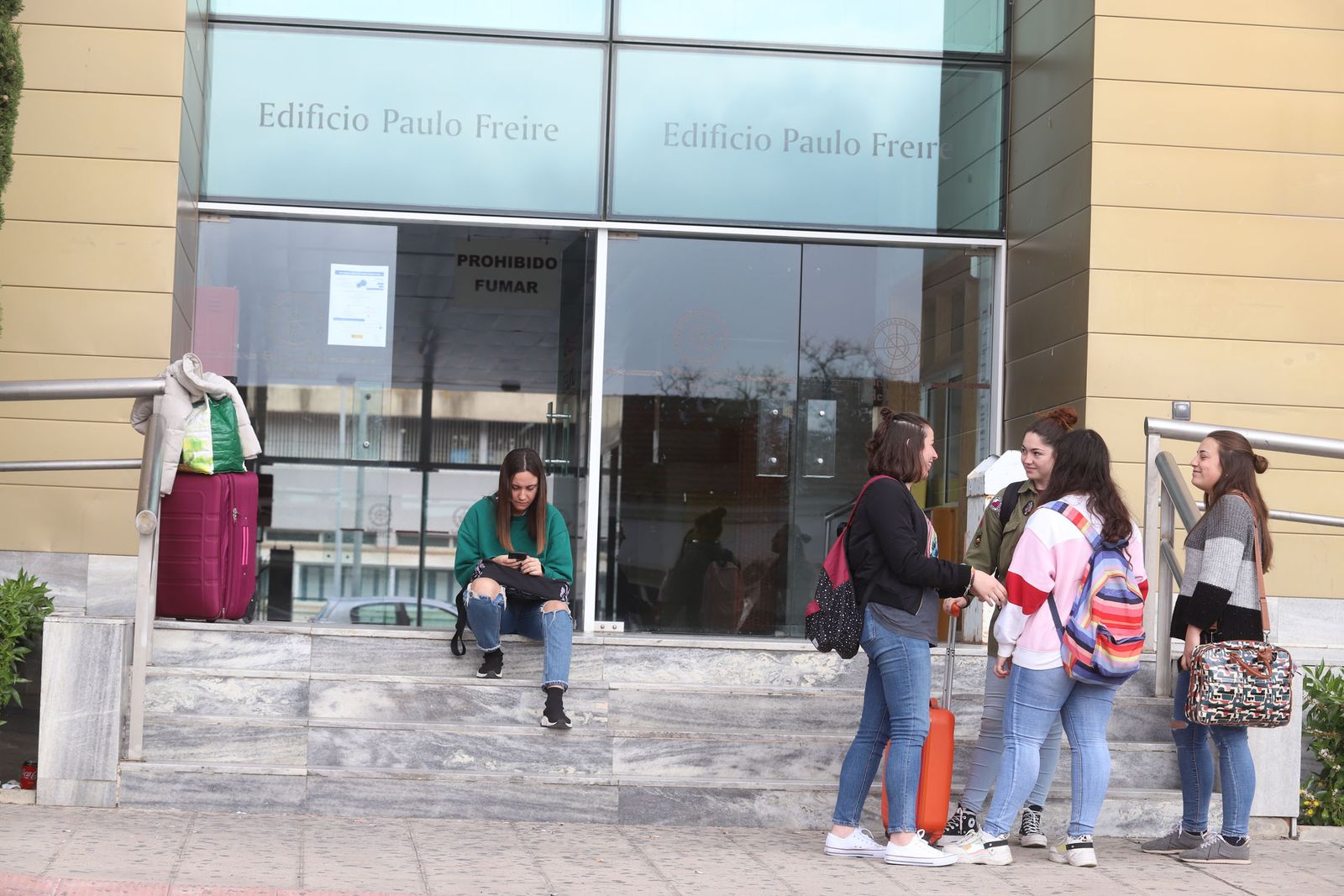 Varias alumnas con maletas conversan en la puerta de una de las dependencias del campus del Carmen de la Universidad de Huelva.