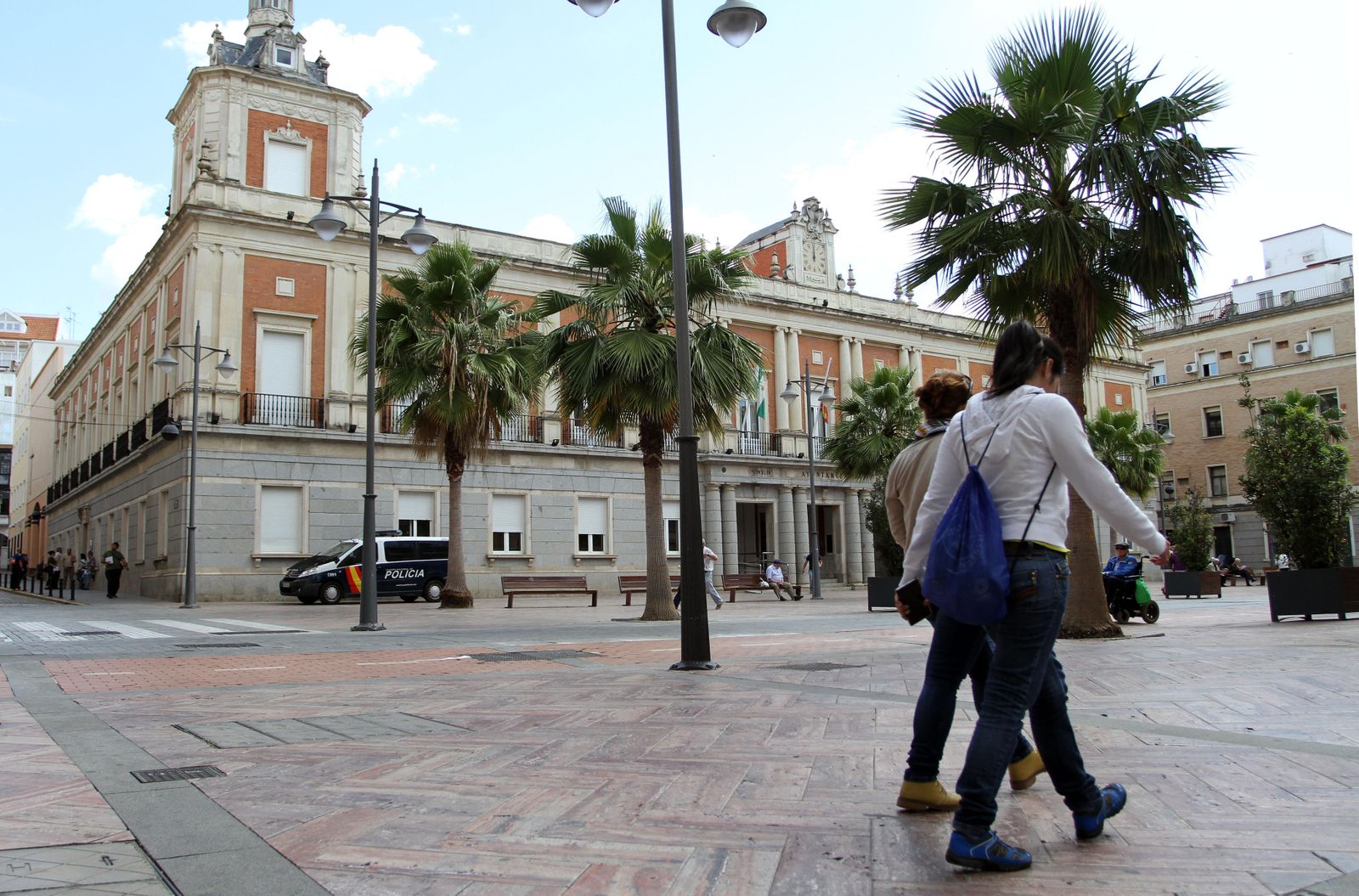 Dos jóvenes a su paso por la plaza de la Constitución con la  fachada del Ayuntamiento capitalino al fondo.