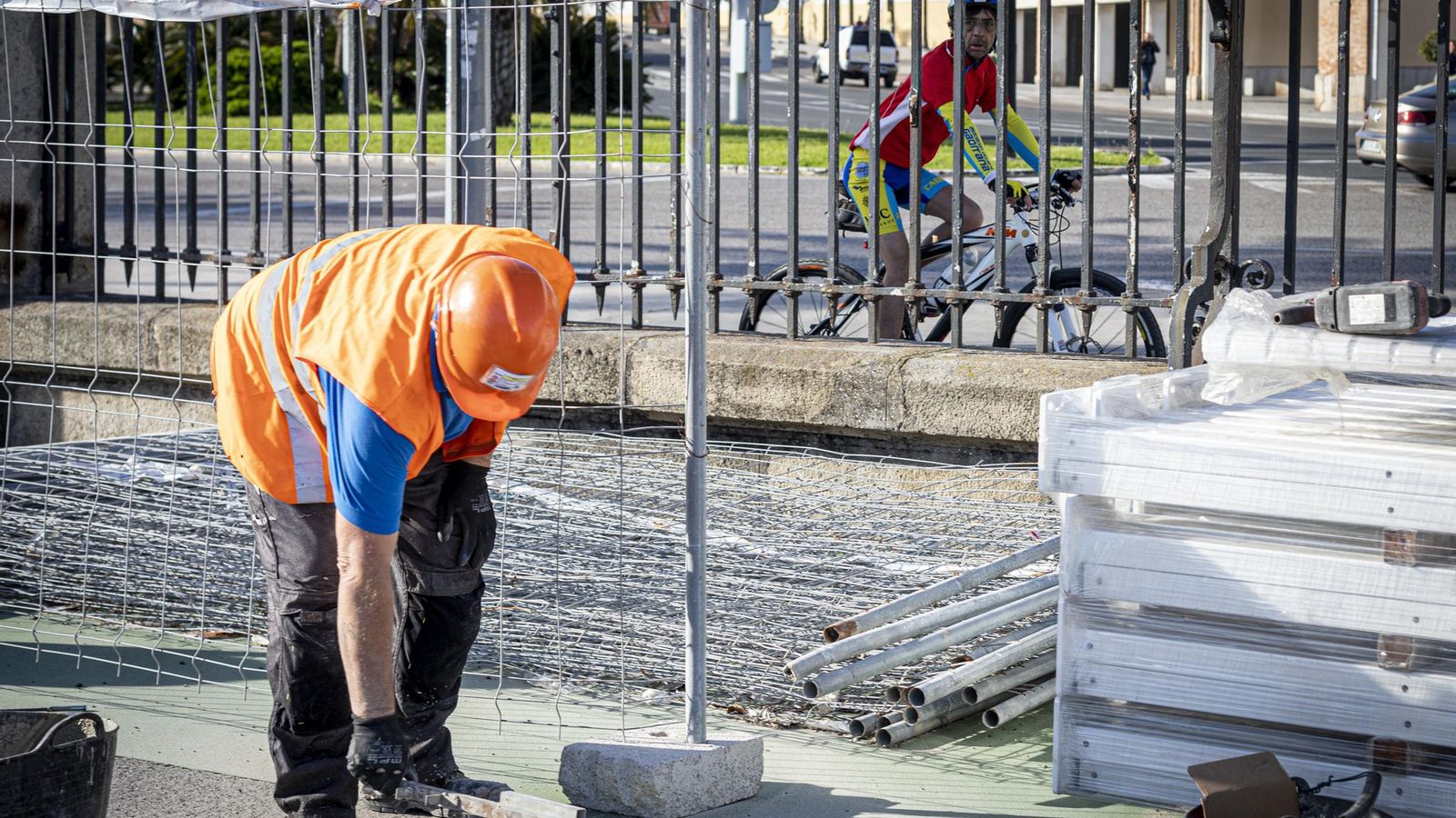 Un ciclista pasa junto a la reja del Muelle y observa cómo se construye el nuevo carril por el interior del Muelle.