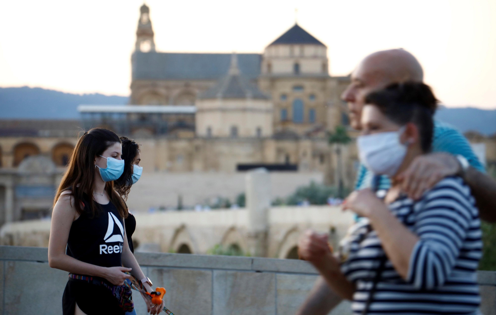 Dos jóvenes circulan con mascarilla por el puente Romano.