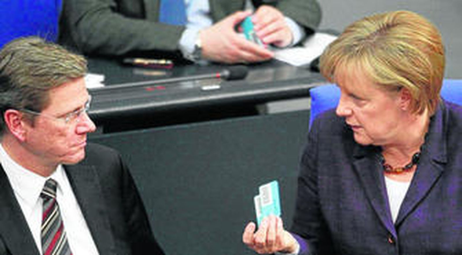 La canciller Angela Merkel sostiene su tarjeta de votación mientras habla con su ministro de Exteriores, el liberal Westerwelle.