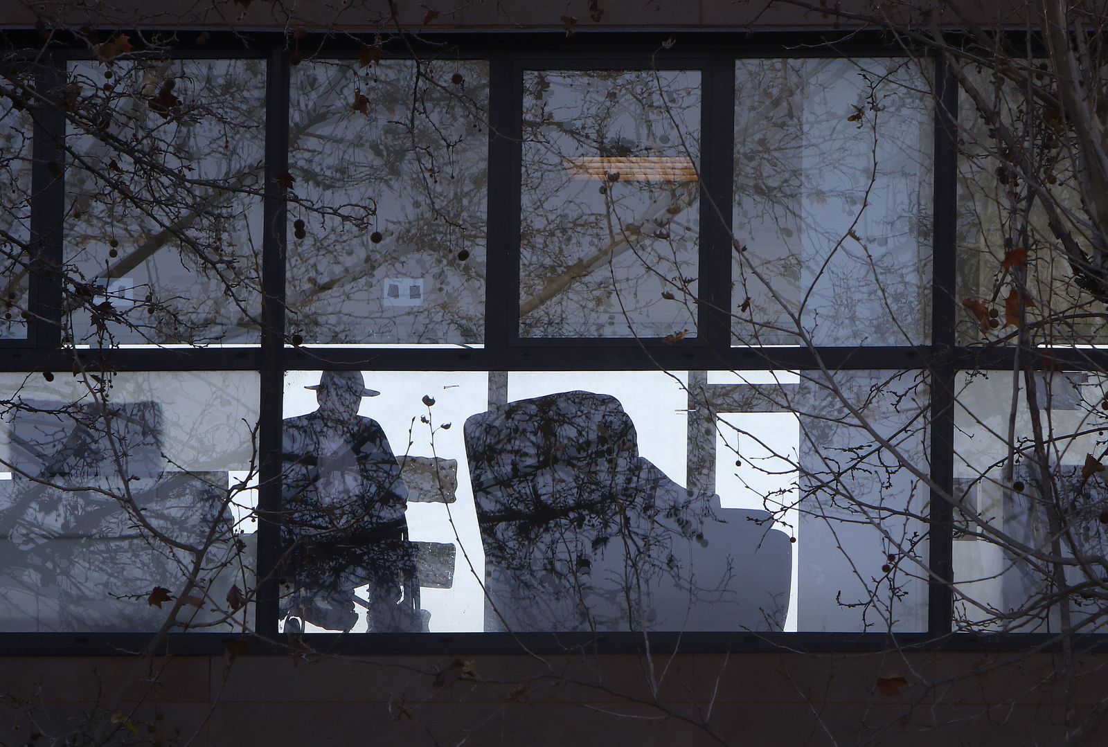 Un anciano mira al exterior tras la cristalera de un centro de mayores.