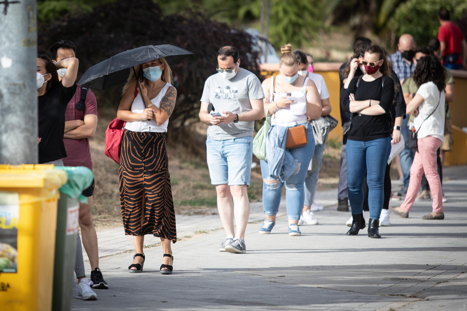 Una mujer se protege del sol con un paraguas en la cola de la vacunación