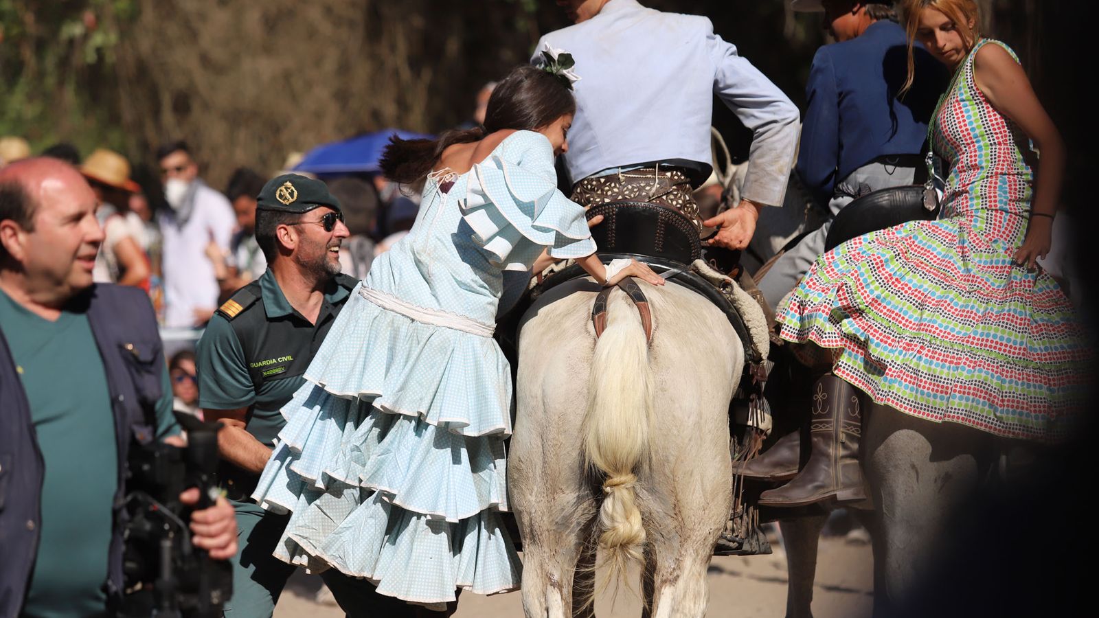 Un agente de la Guardia Civil ayuda a montar a una rociera a la grupa de su caballo.