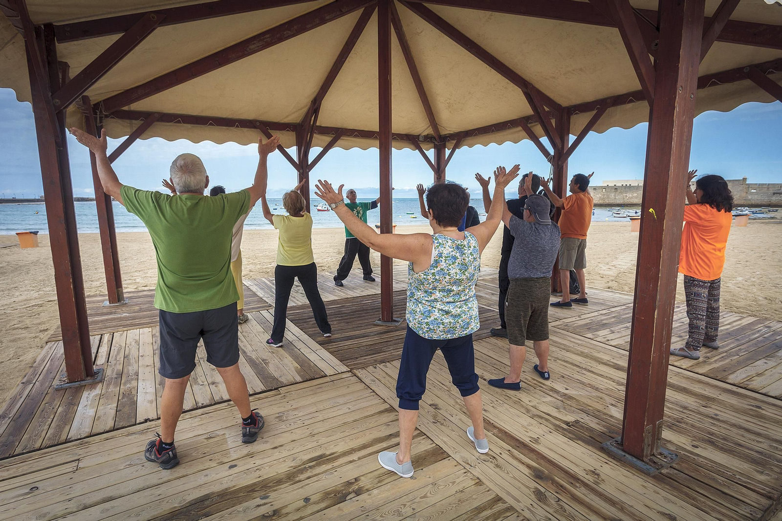 Varias personas participan en una clase de taichí a primera hora en la playa de La Caleta.