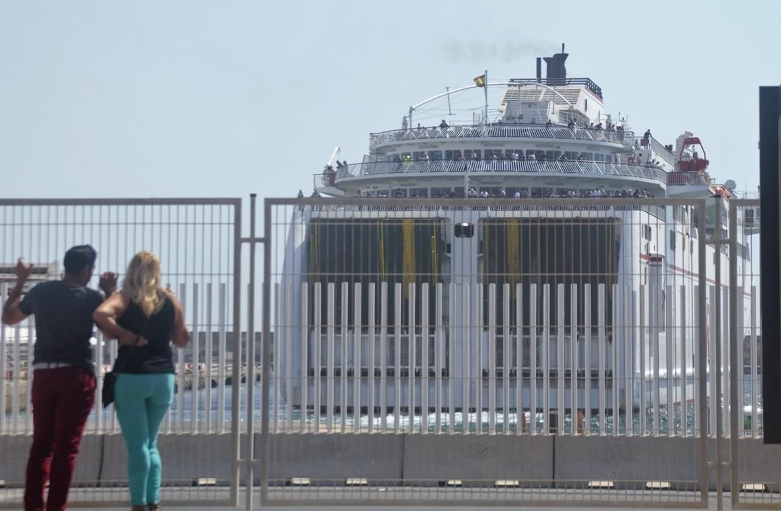 Dos personas observan un ferry repleto de pasajeros a punto de salir del Puerto de Motril