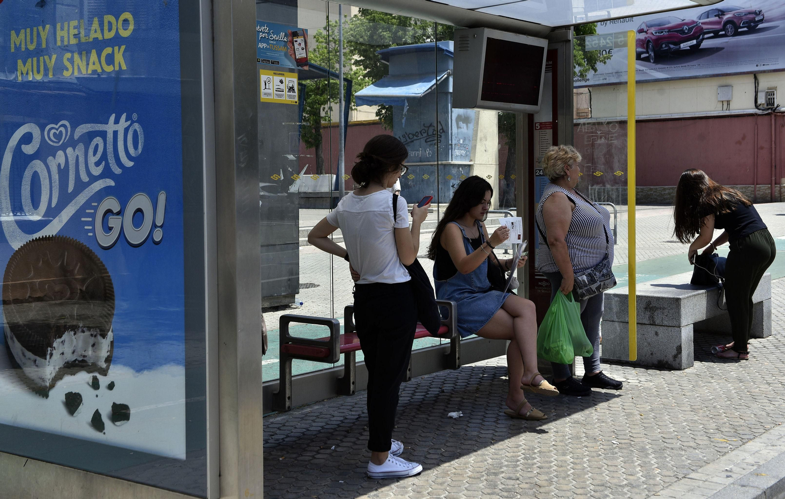 Varias personas aguardan el autobús en una parada.