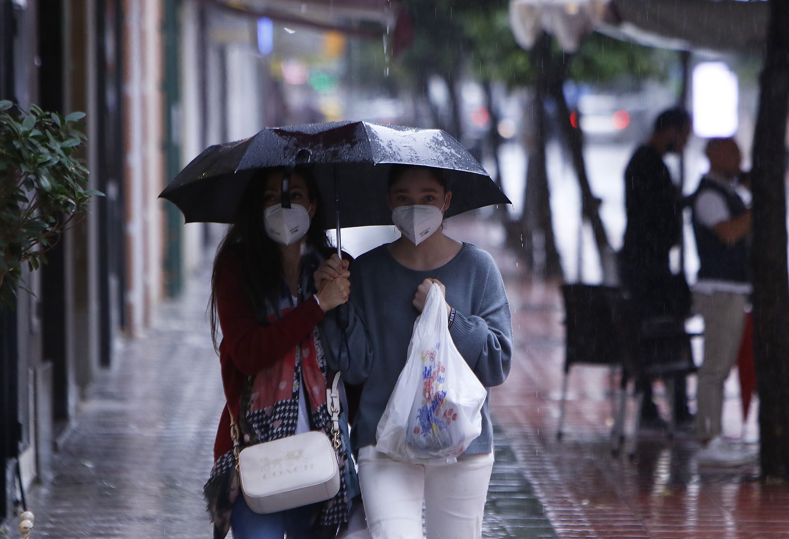 Dos mujeres se refugian de la lluvia bajo un paraguas.