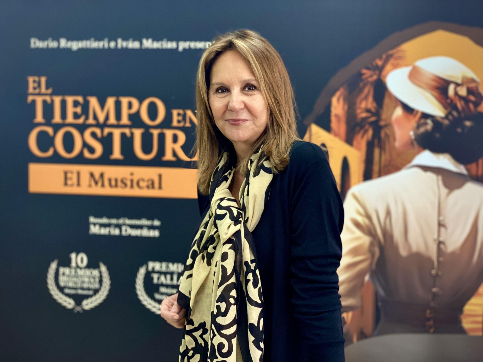 La escritora María Dueñas, con el cartel de 'El tiempo entre costuras. El Musical'.