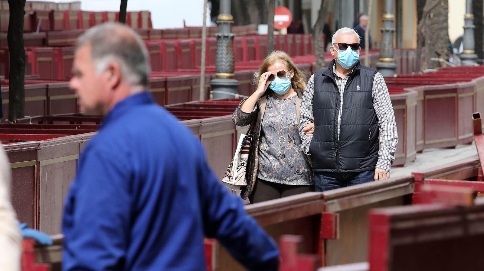 Ciudadanos pasan junto a los palcos de la Carrera Oficial con la mascarilla puesta.