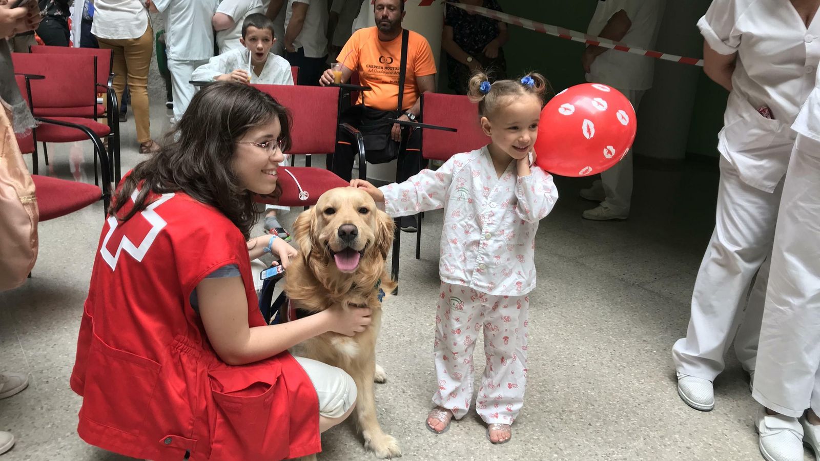 La pequeña Zoe sonríe con su globo junto a una de las voluntarias de Cruz Roja.