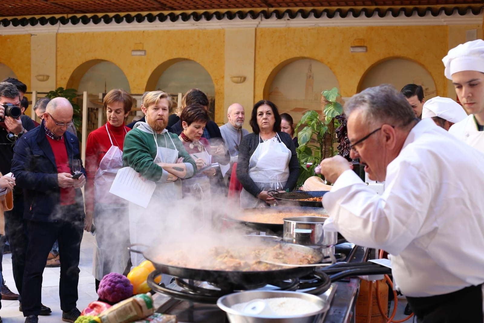 1. Juan Tamarit prueba el arroz ante la atenta mirada de los asistentes. 2. El cocinero valenciano añade arroz a una paella de verduras. 3. Tamarit agrega hebras de azafrán al arroz mientras el público observa.