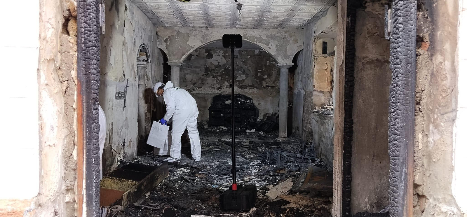 Un agente de Criminalística de la Guardia Civil busca pruebas en el interior de la casa incendiada en Las Gabias