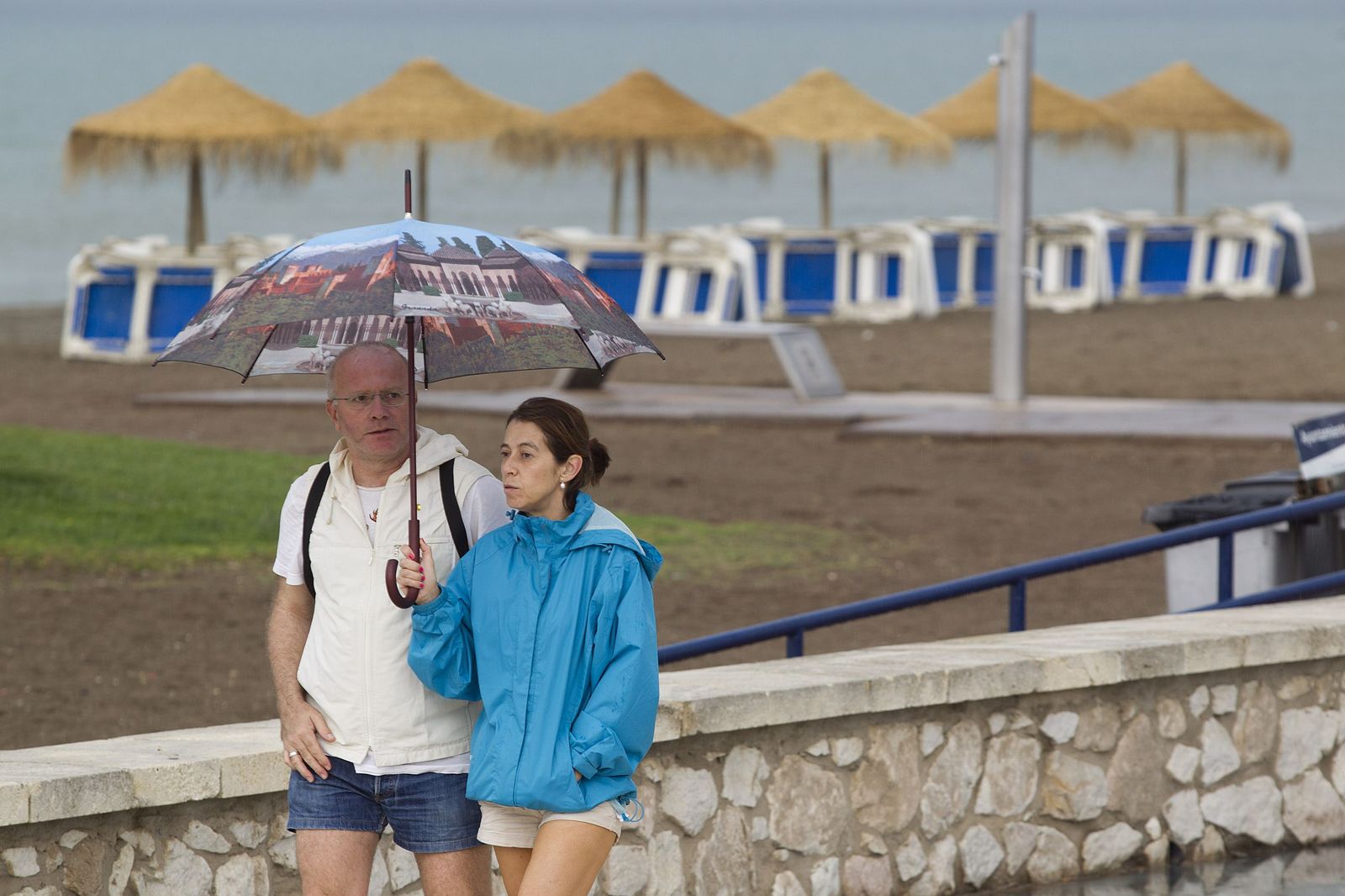 Varias personas caminan con paraguas por el Paseo Marítimo Antonio Banderas de la capital, debido a las lluvias.