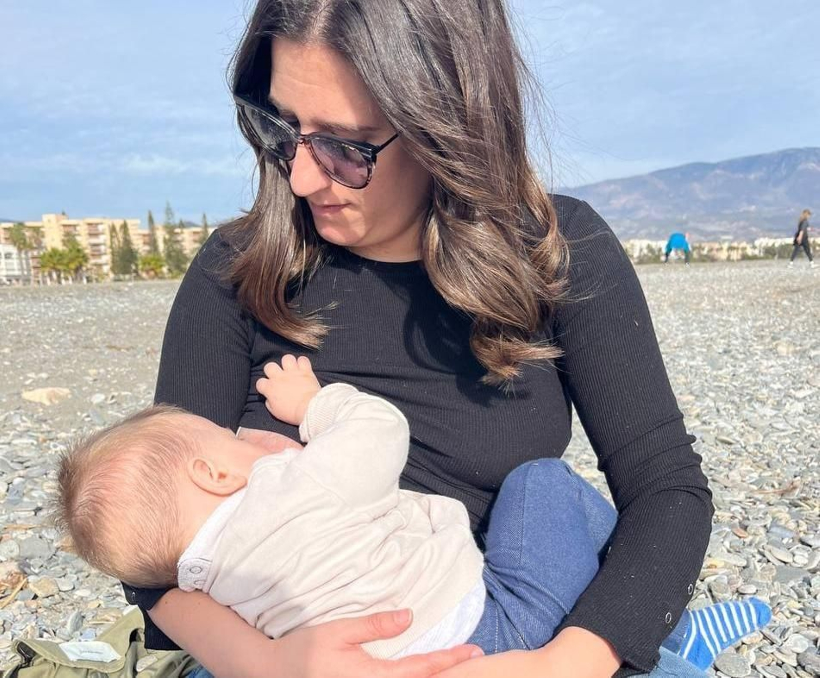 Una mujer da el pecho a su bebé en la playa