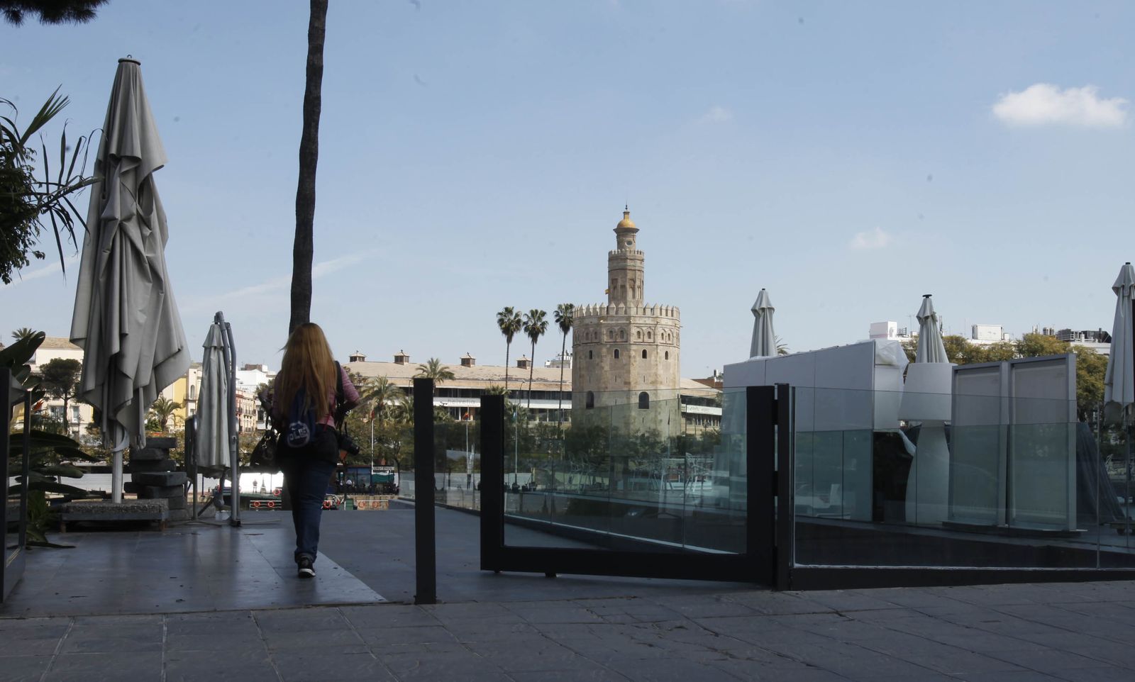 Una joven camina junto a la valla de cristal del restaurante que impide el acceso al río en la calle Betis.