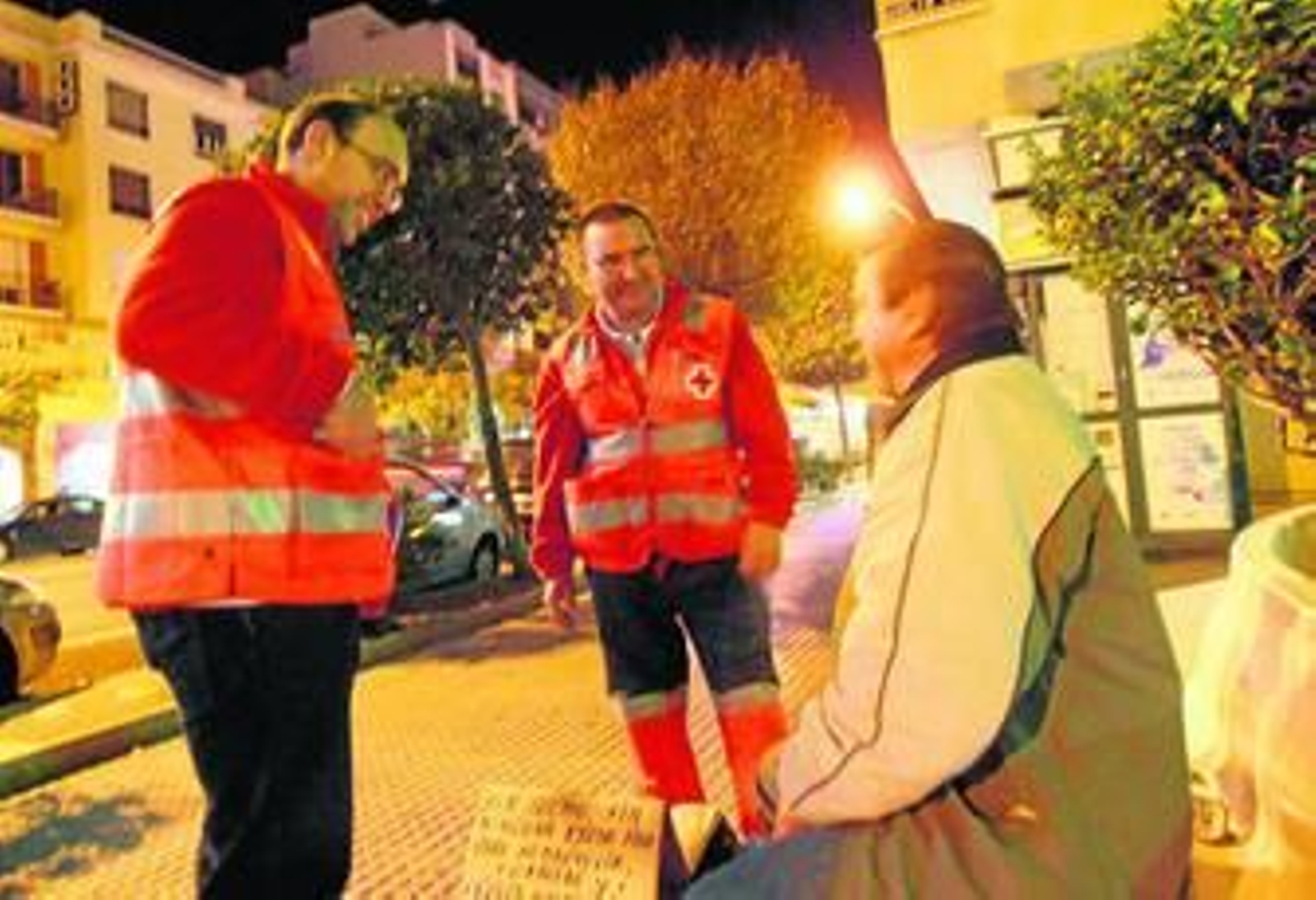 Dos voluntarios de Cruz Roja atienden a una persona en la calle.