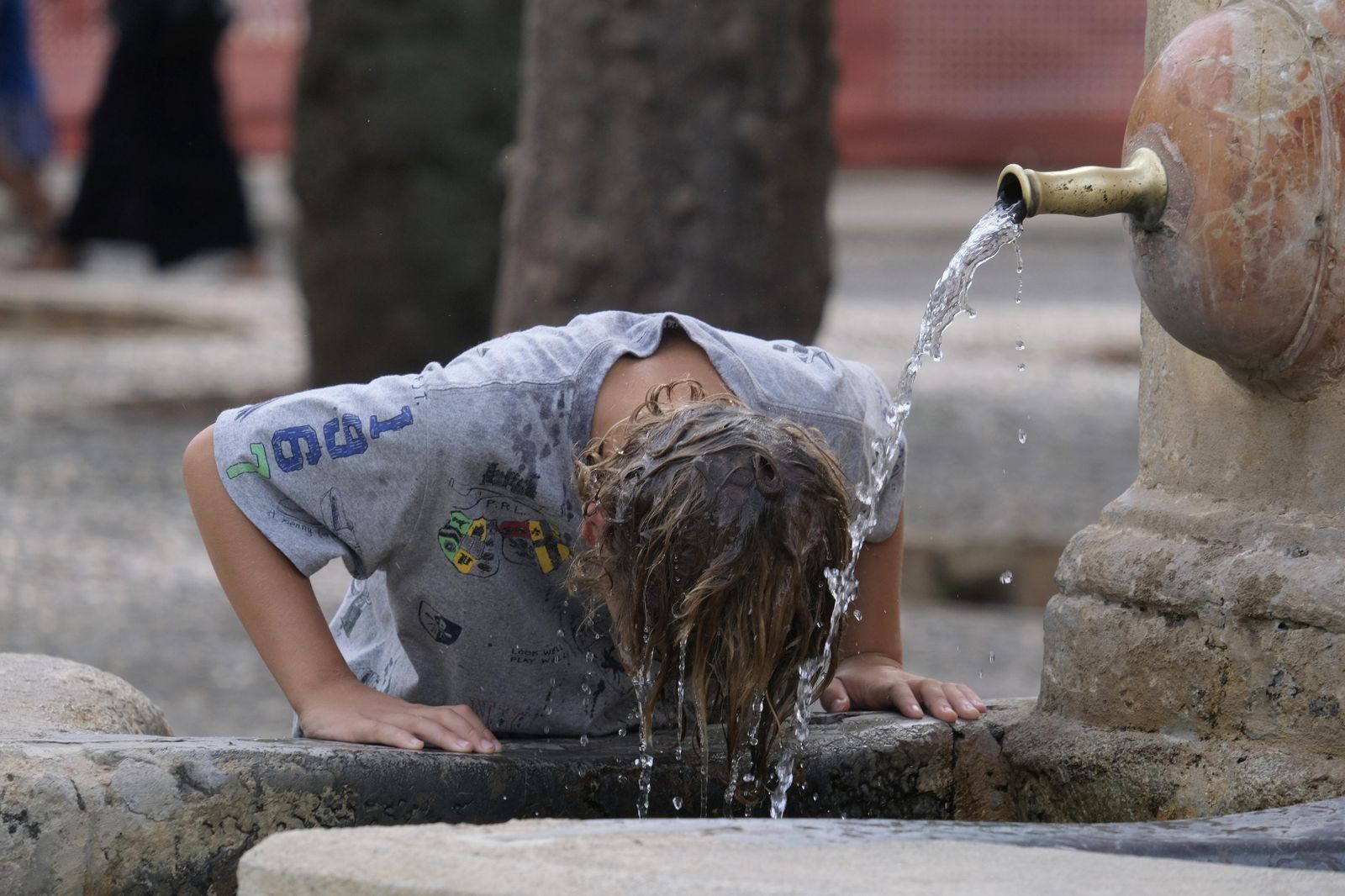 Un joven se moja la cabeza en una fuente para combatir el calor.