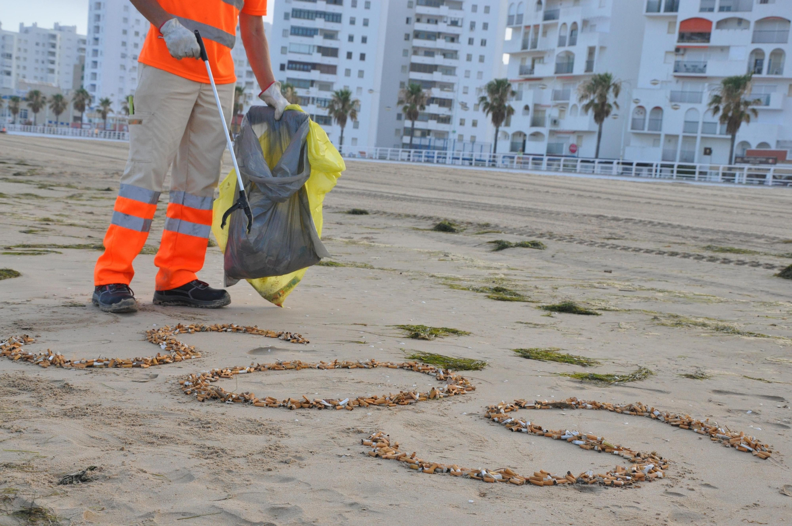 Un operario de la limpieza de playas , recogiendo las colillas  encontradas en la arena.