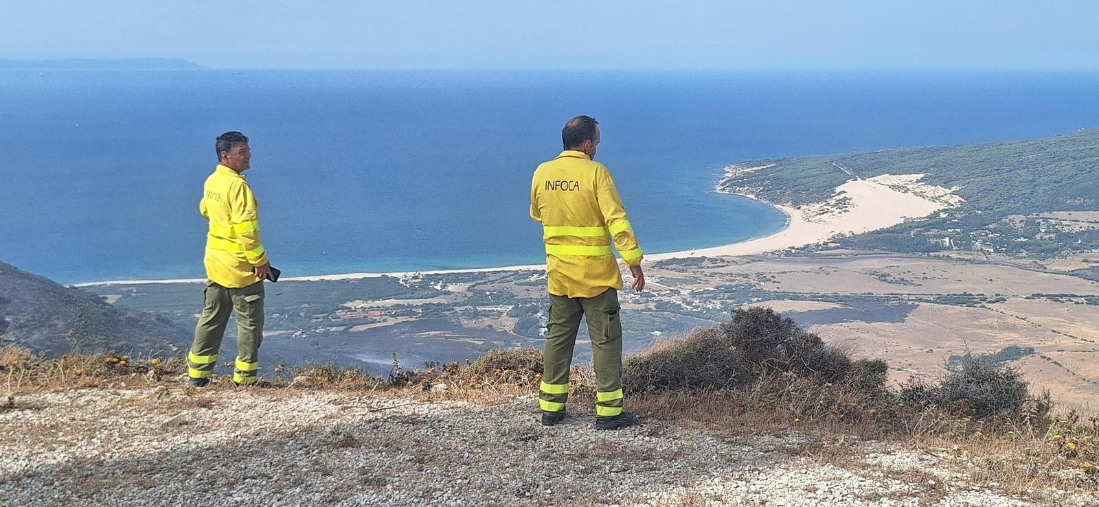 Dos agentes del Plan Infoca observan la zona quemada por el incendio en arifa, con la playa de Valdevaqueros al fondo.