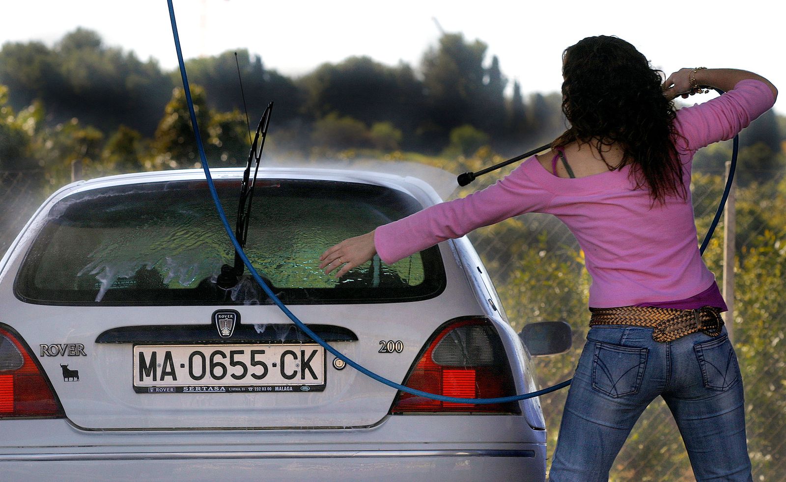 Una mujer lava su coche  a presión con una lanza de agua.