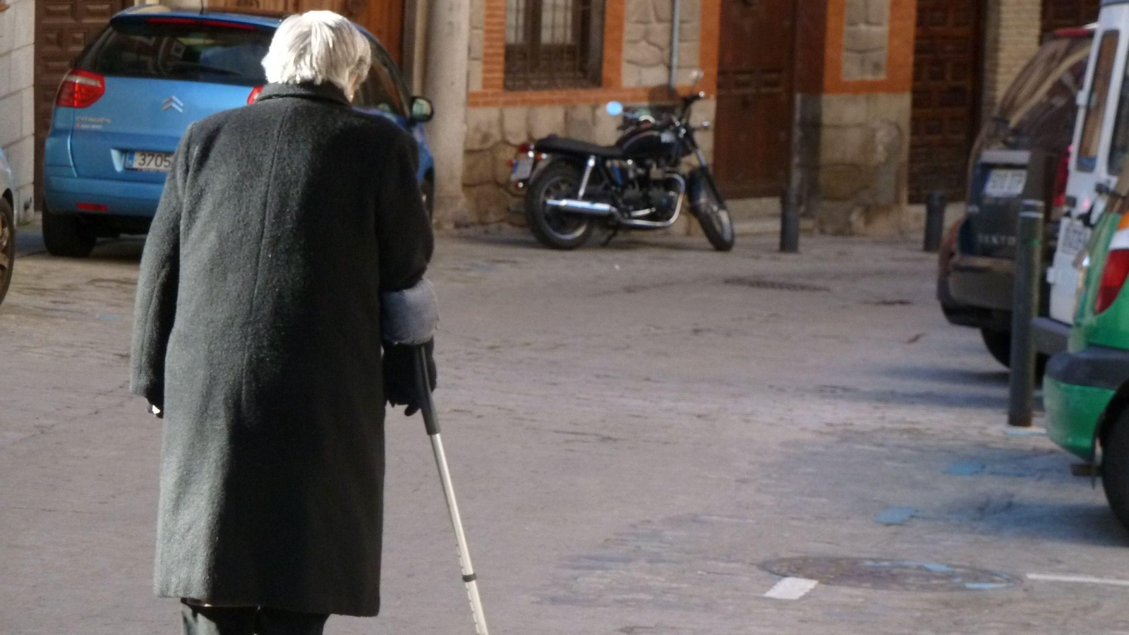 Una anciana camina por la calle ayudada de su muleta