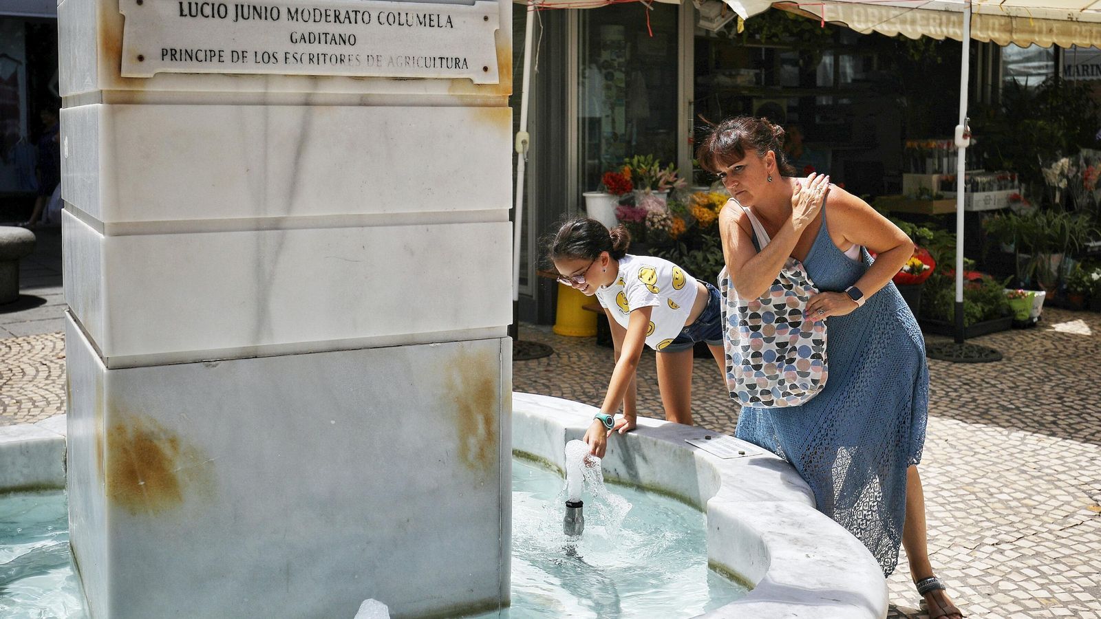 Una mujer y una niña se refrescan en la fuente de la Plaza de Las Flores.