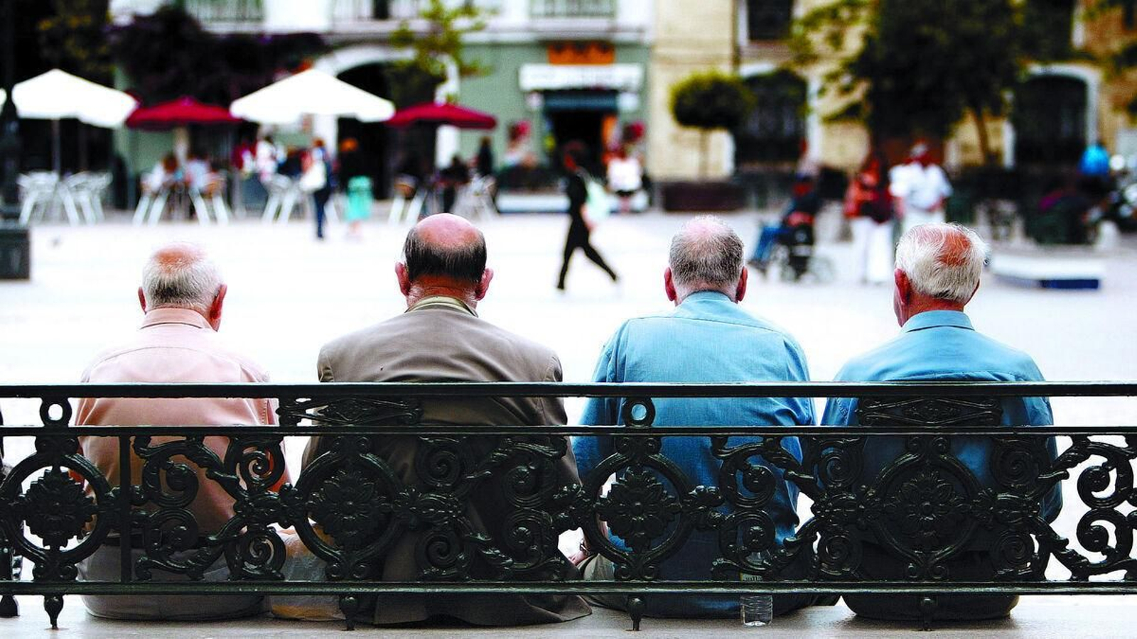 Un grupo de hombres mayores sentados en un banco en una plaza pública. Un grupo de hombres mayores sentados en un banco en una plaza pública.