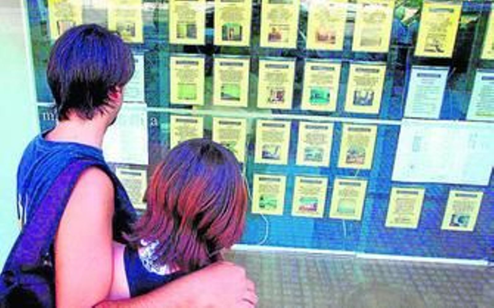 Dos jóvenes miran los anuncios de una agencia inmobiliaria.