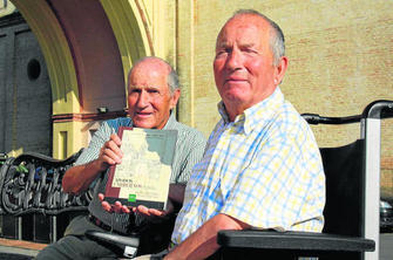 José Manuel (izquierda) y Francisco posan con su libro frente al conocido arco de Umbrete.