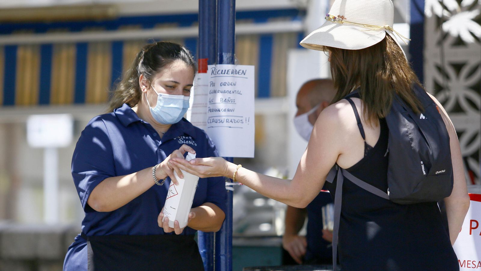 Una camarera de un chiringuito ofrece gel hidroalcohólico a una cliente.