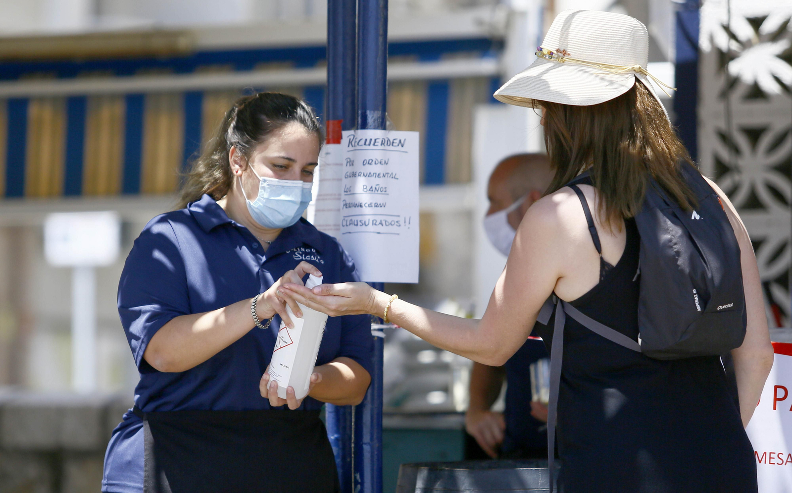 Una camarera de un chiringuito ofrece gel hidroalcohólico a una cliente.
