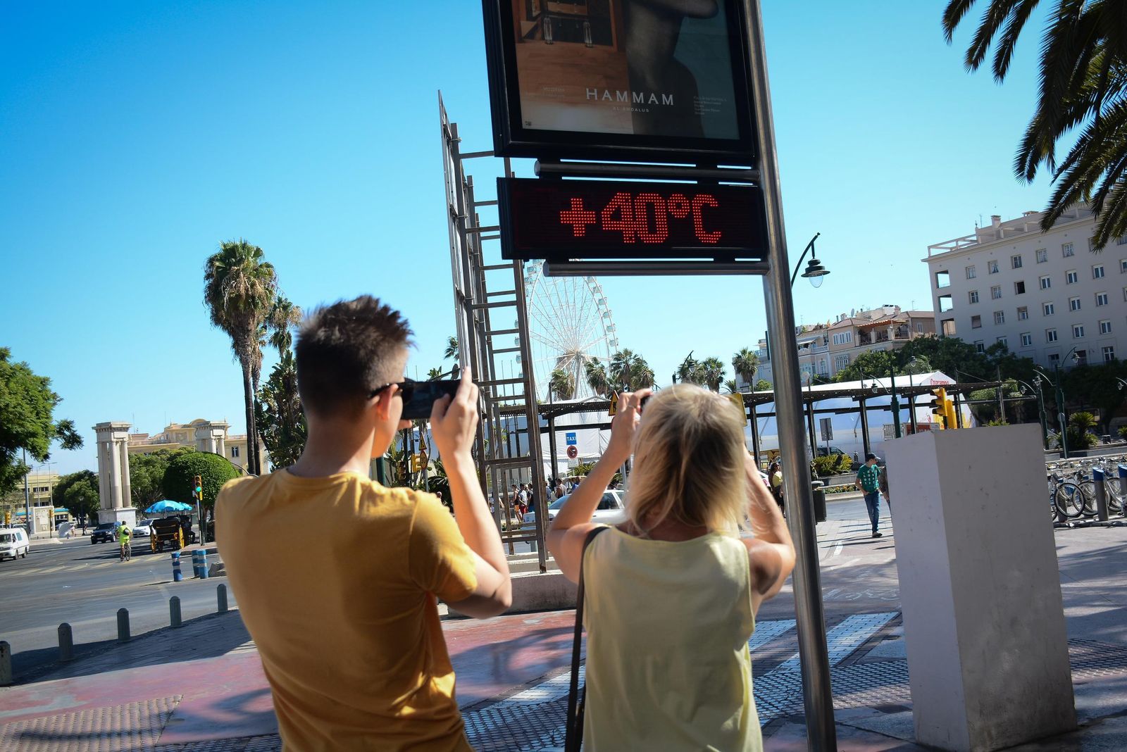 Dos turistas hacen fotos del termómetro  de la Plaza de la Marina.